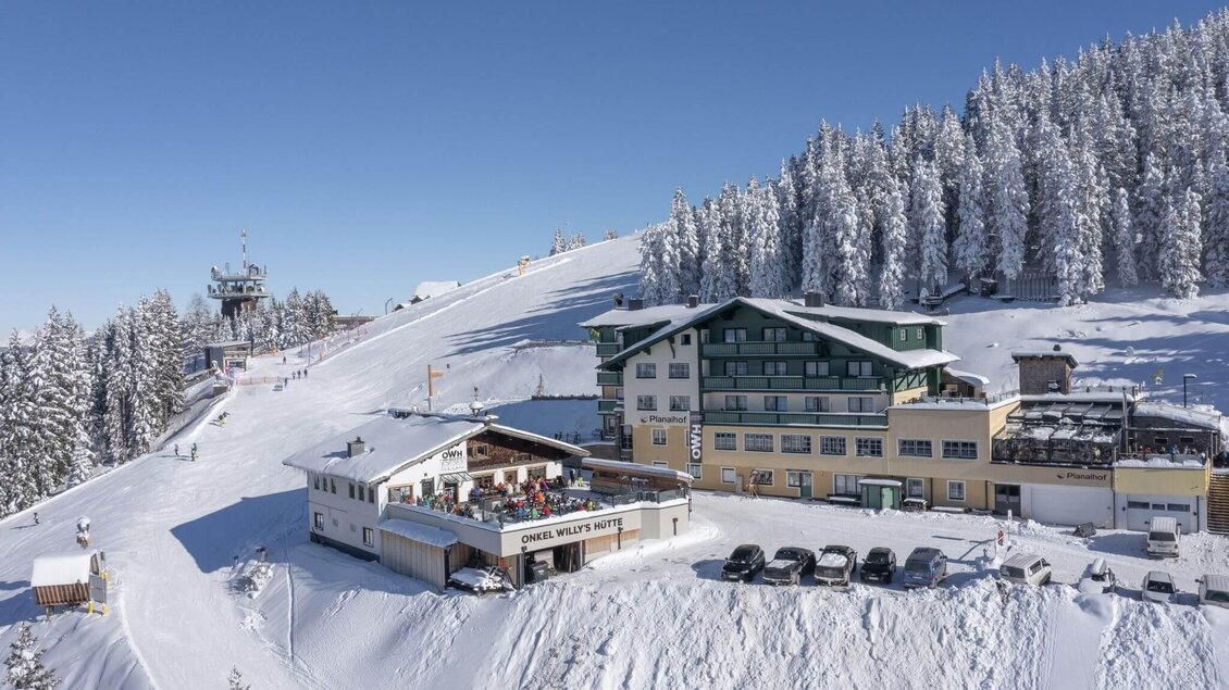 Ein schneebedecktes Berggebiet mit einem Gebäude im Vordergrund. Der Himmel ist klar und blau, umgeben von verschneiten Bäumen. | © Planaihof, Max Eisl