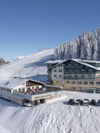 A snow-covered mountain area with a building in the foreground. The sky is clear and blue, surrounded by snow-covered trees. | © Planaihof, Max Eisl