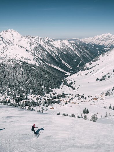 A snow-covered mountain landscape with high peaks and a clear blue sky. Two skiers are skiing over the untouched slopes. | © Armin Walcher