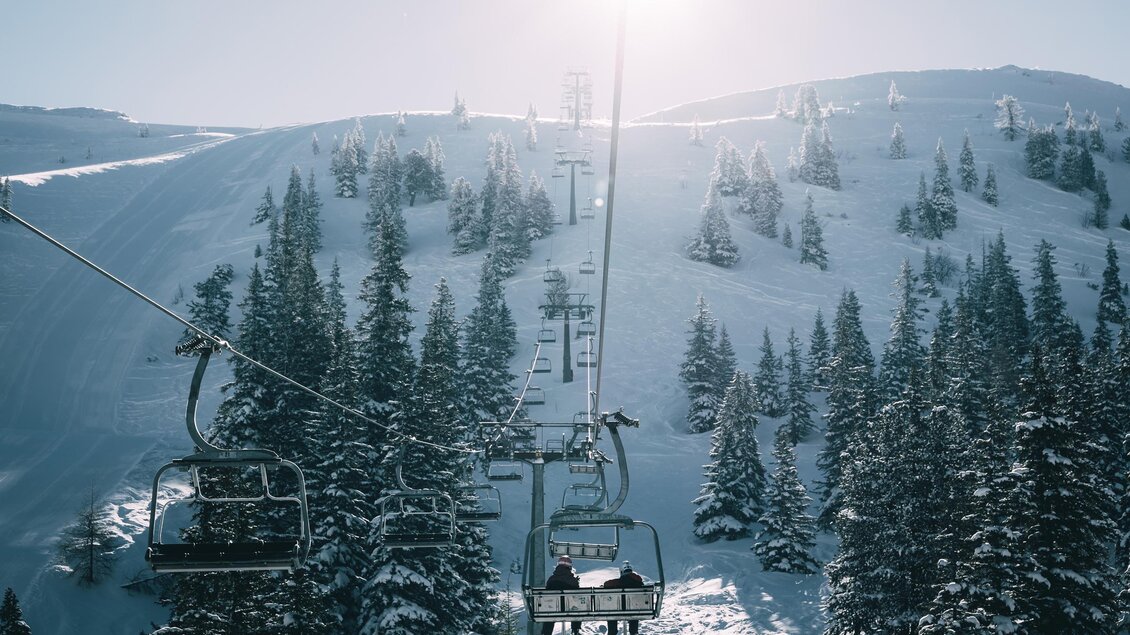 Eine Skiliftfahrt durch eine verschneite Landschaft mit hohen, grünen Tannen. Der klare Himmel und die sonnenbeschienene Bergwelt schaffen eine winterliche Atmosphäre. | © Armin Walcher