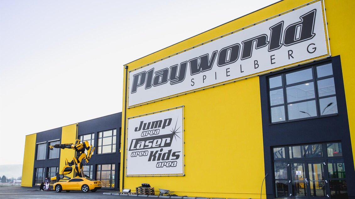 Ein großes, gelbes Gebäude mit dem Schriftzug "Playworld Spielberg". An der Fassade sind verschiedene Attraktionen wie "Jump", "Laser" und "Kids" angezeigt. | © Playworld Spielberg