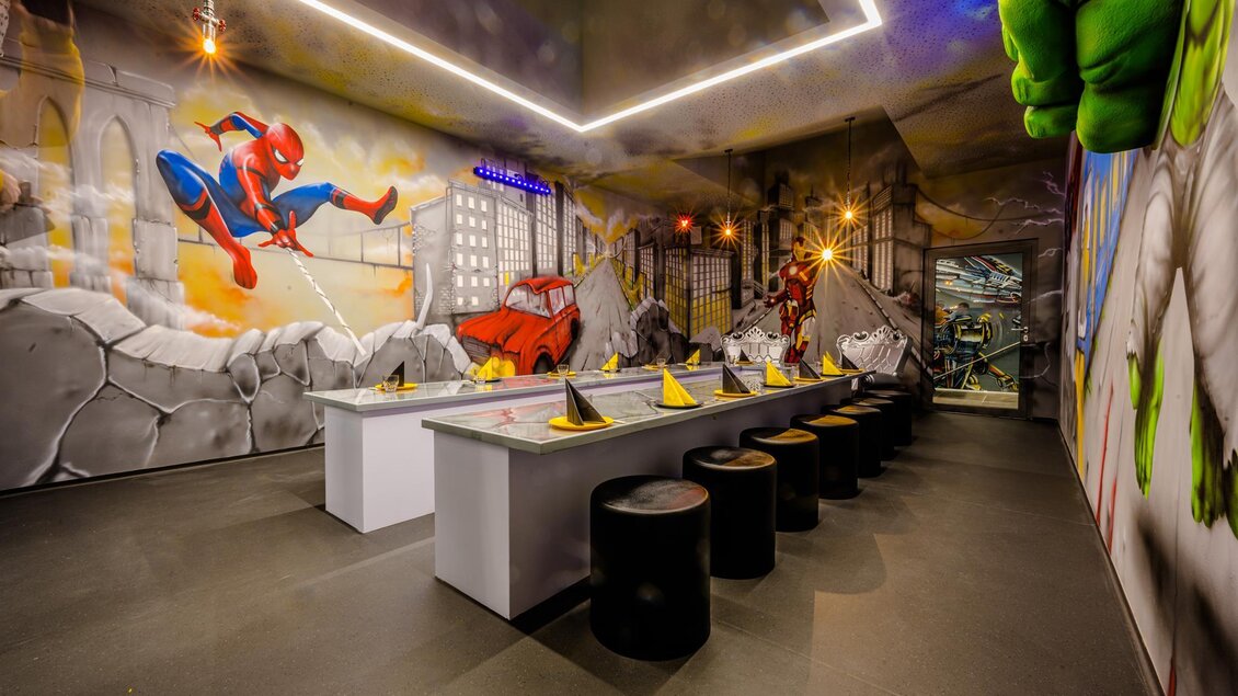 Ein kreativer Raum mit einer Eiswaffel-Tischanordnung und farbenfrohen Wandmalereien. Die dargestellten Superhelden schaffen eine lebendige und spielerische Atmosphäre. | © Playworld Spielberg