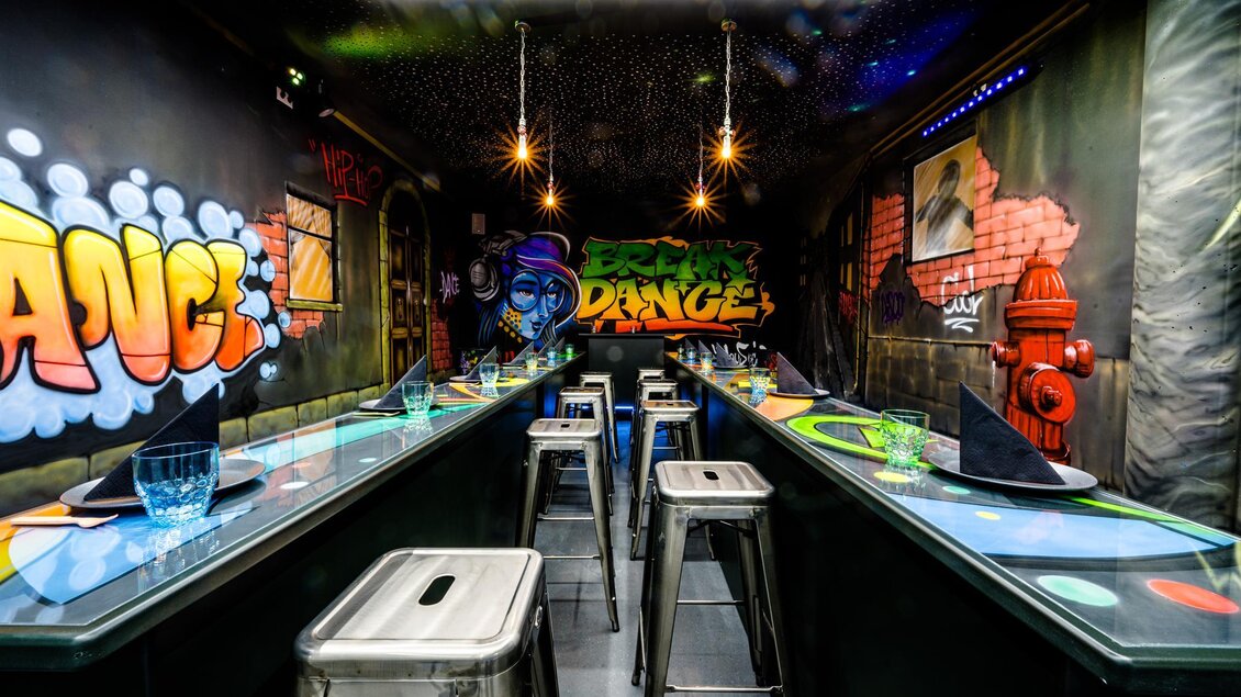 Ein modernes Restaurant mit Graffiti-Wänden und stilvollen Barhockern. Die Anordnung der Tische und das schicke Ambiente schaffen eine einladende Atmosphäre. | © Playworld Spielberg