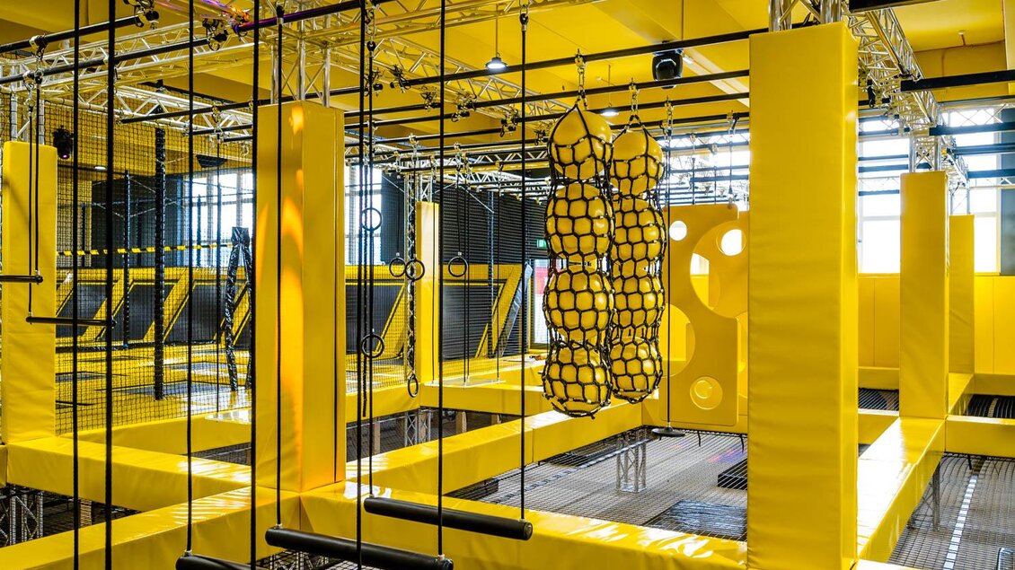 Ein modernes Trampolin- und Kletterzentrum mit gelben Wänden und verschiedenen Kletterelementen. Die Einrichtung bietet spannende Möglichkeiten für aktiven Spaß und Bewegung. | © Playworld Spielberg