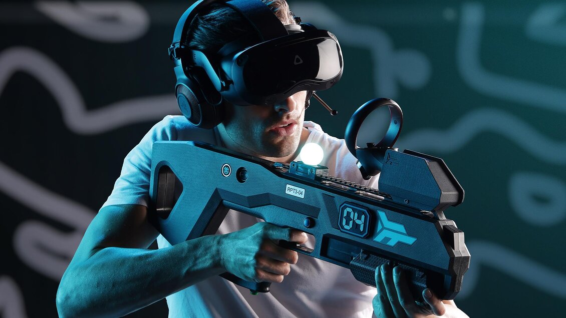 Ein Mann trägt eine VR-Brille und hält ein futuristisches Gewehr. Er scheint in ein virtuelles Spiel vertieft zu sein. | © Playworld Spielberg