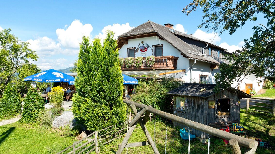 Ein gemütliches Gästehaus umgeben von Bäumen und einer großen Wiese. Auf der Terrasse stehen blauen Sonnenschirme bereit für Gäste. | © TV Region Graz - René Vidalli