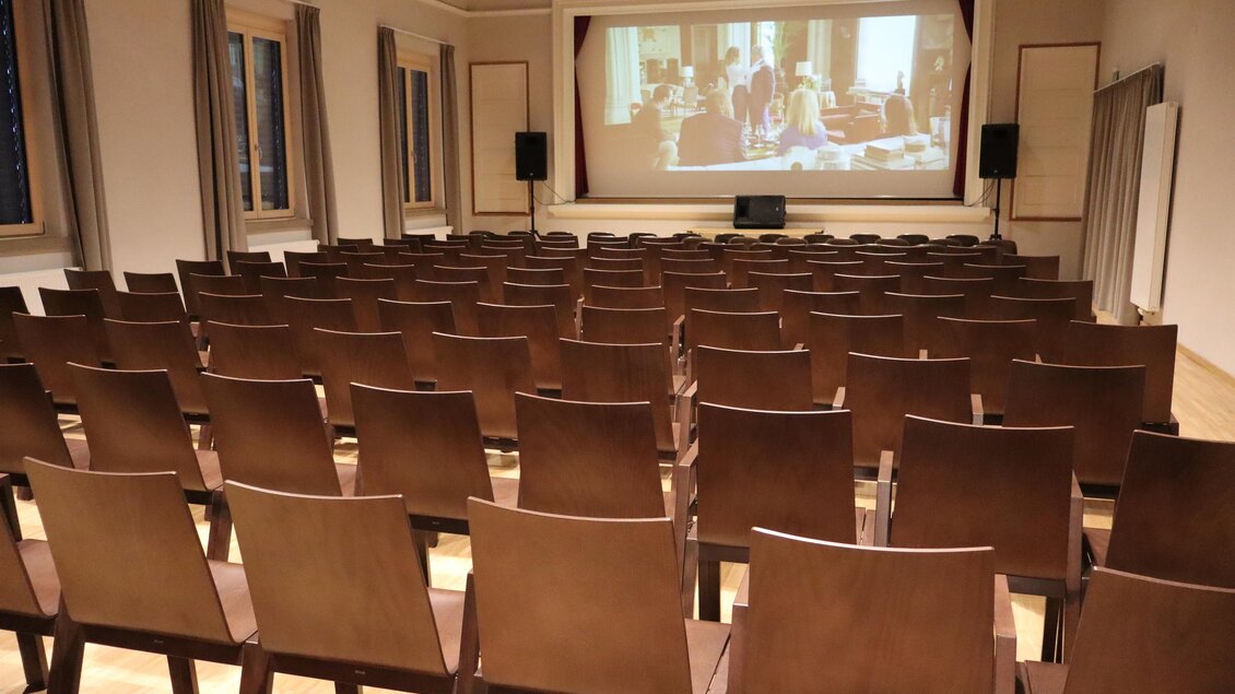 Ein leerer Veranstaltungsraum mit vielen Stühlen und einer Leinwand im Hintergrund. Der Raum ist hell erleuchtet und bereit für eine Präsentation oder Veranstaltung. | © Karin Mauser