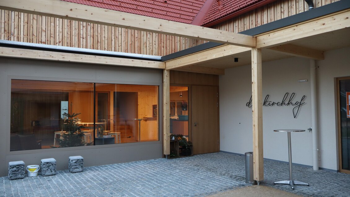 Ein moderner Eingangsbereich mit Holzverkleidung und großen Fenstern. Die Fliesen und der Holzüberstand schaffen ein einladendes Ambiente. | © Karin Mauser