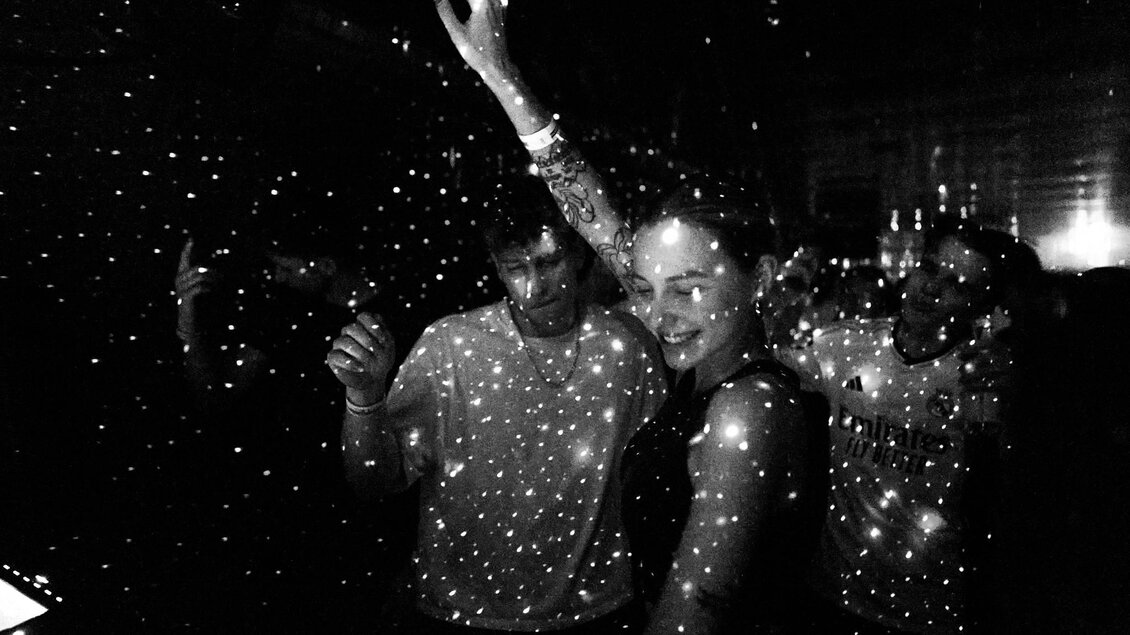 Schwarz-Weiß-Aufnahme von Menschen, die in einem dunklen Raum tanzen, umgeben von Lichtpunkten, die wie Sterne im Raum wirken | © Postgarage - Stefan Leitner