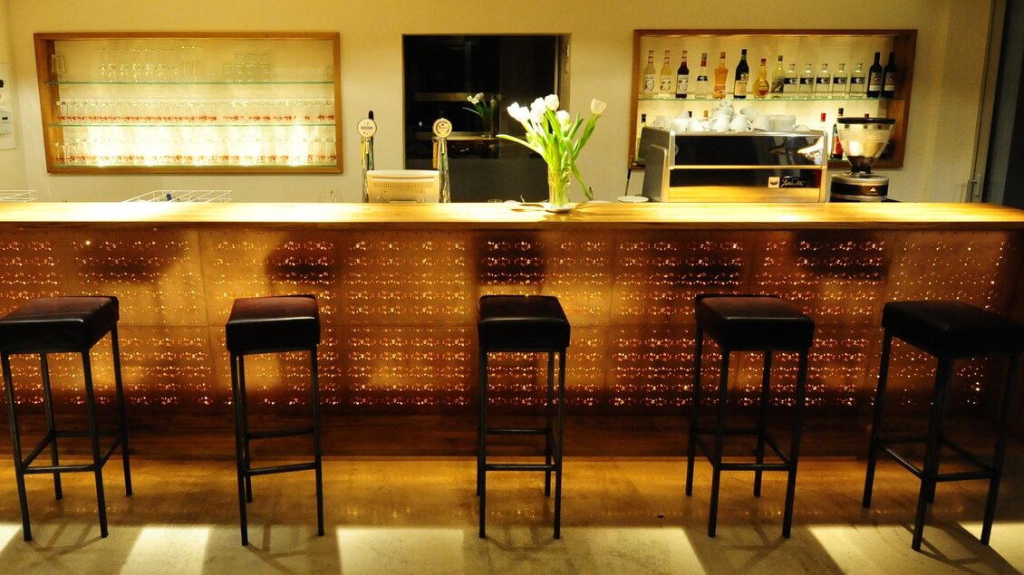 Beleuchteter Bartresen mit Hockern und Flaschenregal | © Postgarage - Elmar Gubisch
