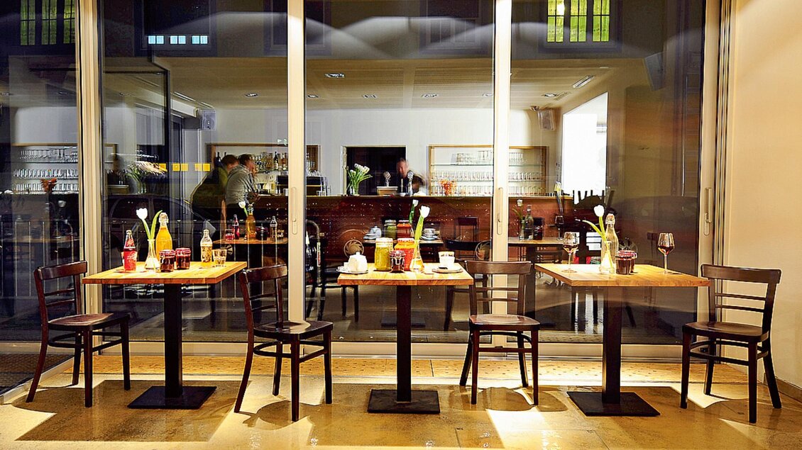 Blick auf Tische mit Getränken im Café der Postgarage Graz, dahinter beleuchtete Bar | © Postgarage - Elmar Gubisch