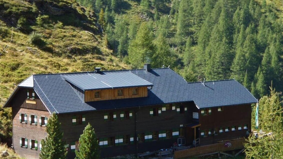 <p>Eine BErghütte im Berggebiet, umgeben von grünen Bäumen. Die Architektur ist dunkel und harmoniert gut mit der natürlichen Umgebung.</p> | © Höflehner Wolfgang