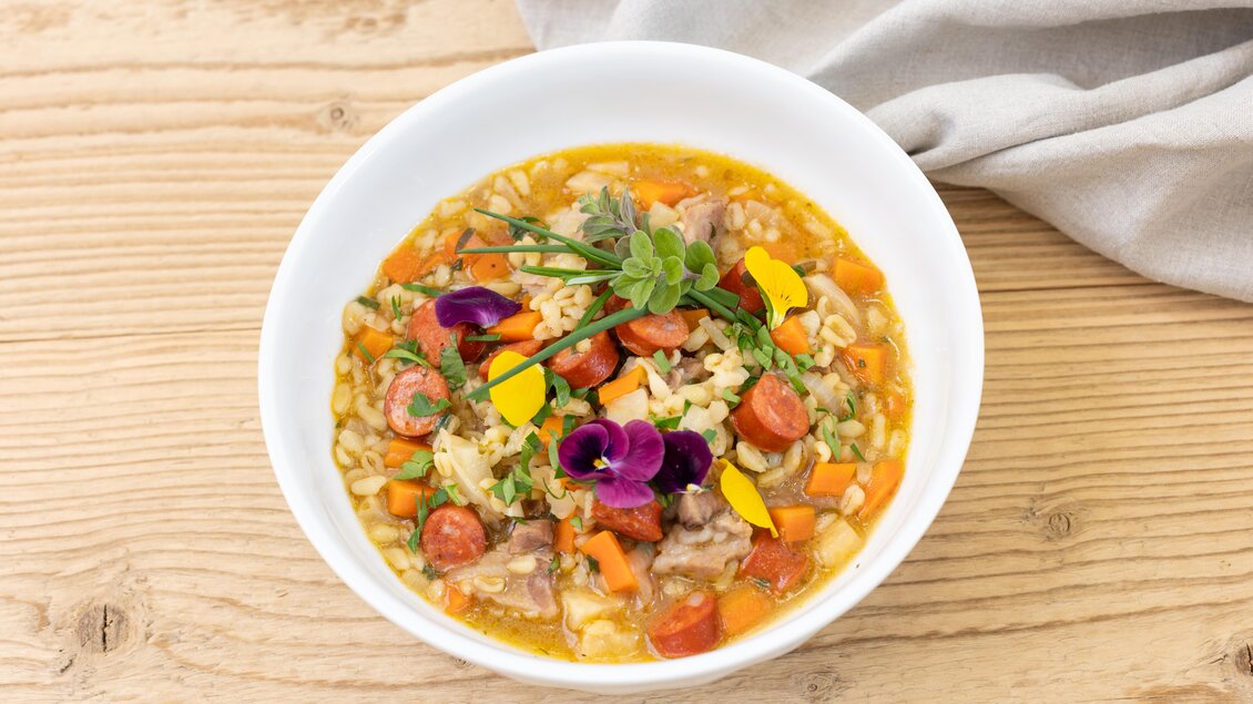 Ein schmackhaftes Gericht mit Reis, Gemüse und Fleisch, garniert mit essbaren Blüten. Das Essen wird in einer weißen Schüssel serviert und steht auf einem Holztisch. | © ©Martin Huber