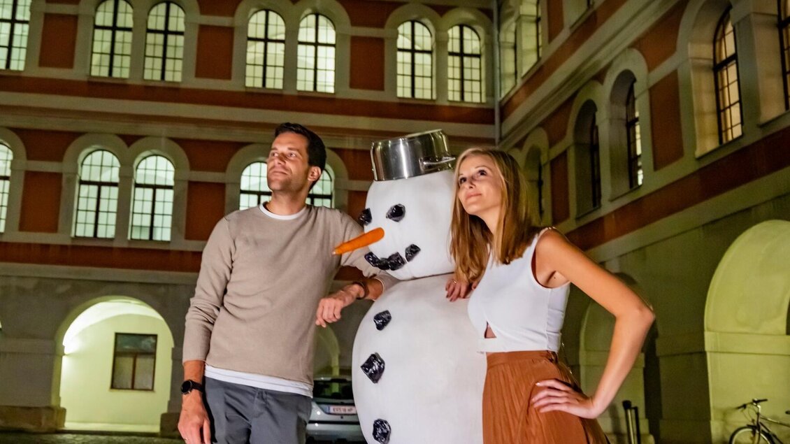 Zwei Personen posieren abends mit Schneemann im beleuchteten Innenhof des Priesterseminars Graz. | © Graz Tourismus-Werner Krug