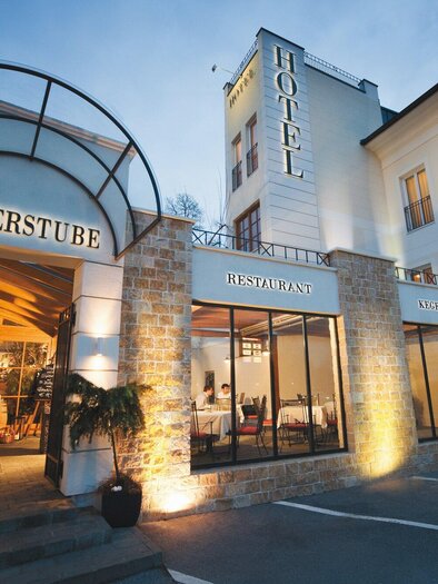 The image shows the entrance of a hotel with the inscription "Römerstube". The façade is illuminated and features modern architecture. | © Römerstube