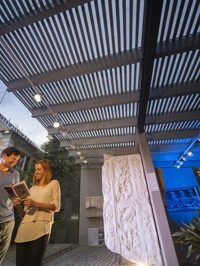 Zwei Personen stehen in einem modernen Ausstellungsraum und betrachten ein Buch. Im Hintergrund sind Skulpturen und eine helle, einladende Architektur zu sehen. | © Bernhard Bergmann