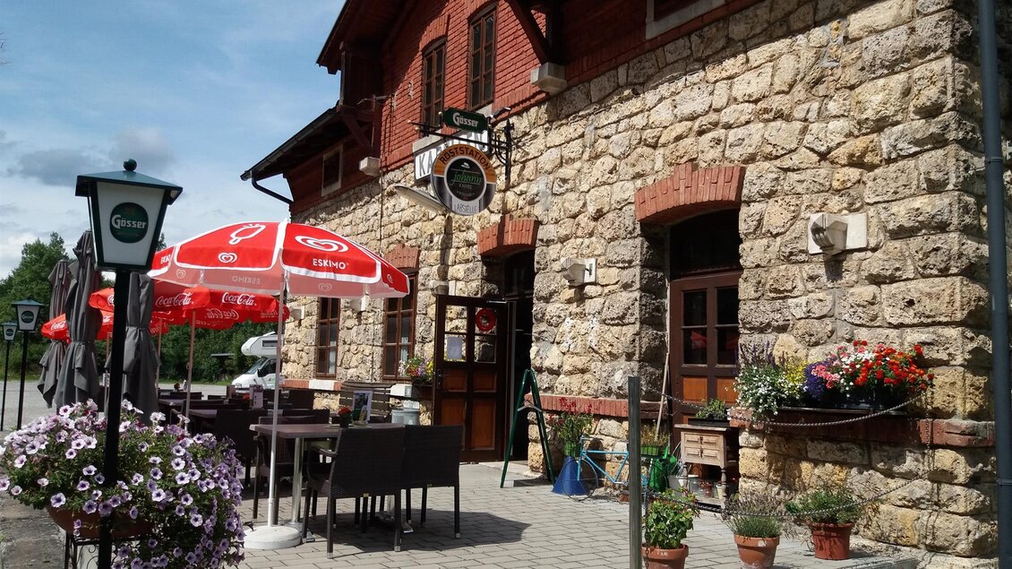 Ein gemütliches Café mit einer Steinfassade und roten Sonnenschirmen. Blühende Pflanzen und Tische im Freien schaffen eine einladende Atmosphäre. | © Röststation