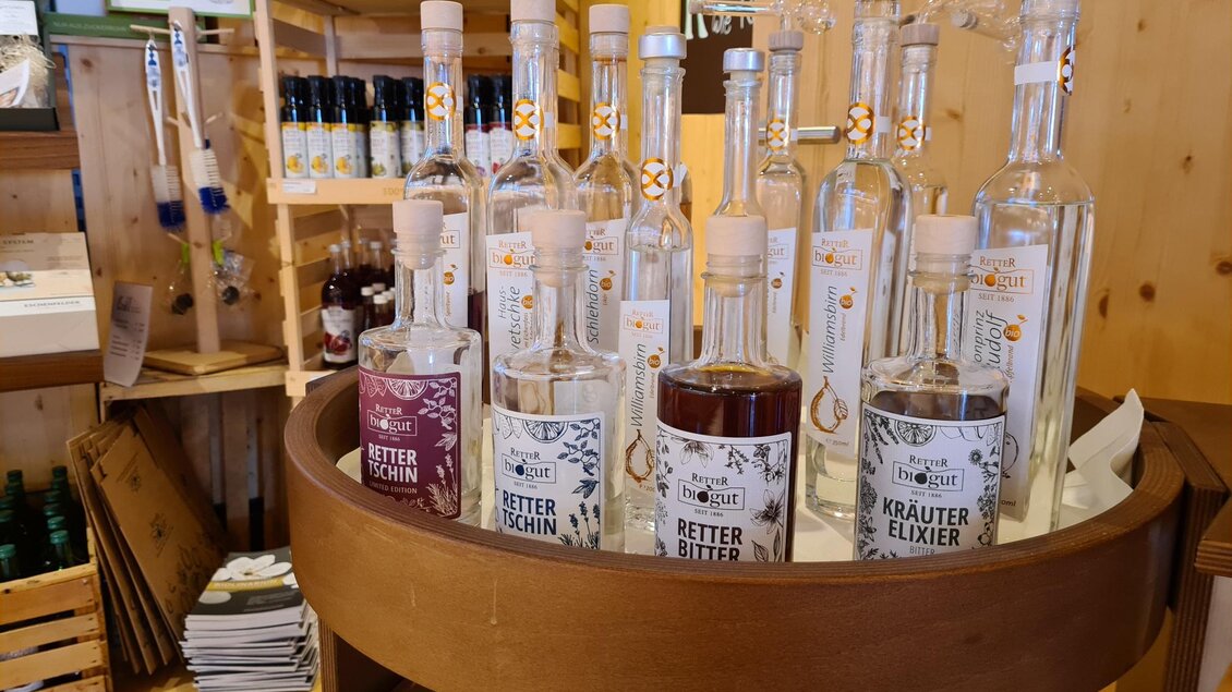 Ein Holzregal mit verschiedenen Flaschen von Kräuterlikören und Schnäpsen. Die Produkte sind bunte Etiketten und stehen auf einem runden Holzgestell. | © Tourismusverband Oststeiermark