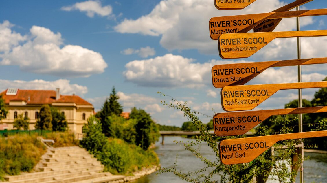 Ein schöner Fluss mit einem Schild, das auf verschiedene Orte hinweist. Über dem Wasser sind einige Wolken am Himmel zu sehen. | © Thermen- & Vulkanland
