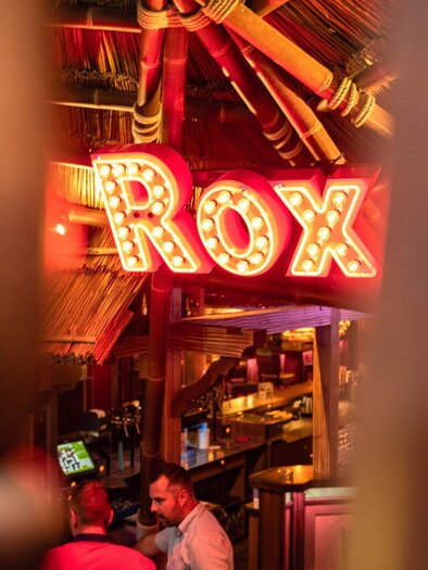 A cozy interior with a neon-lit bar called "Rox". The atmosphere is inviting and designed to be tropical. | © ROX - Kyrillos Mikhail