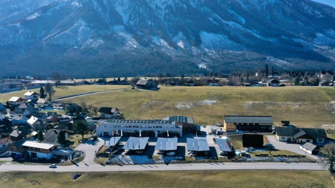 Eine ruhige Landschaft mit einem kleinen Dorf und flachen Häusern. Im Hintergrund erhebt sich ein majestätischer Berg. | © Radhaus, Bad Aussee, Luftaufnahme (c) Markus Raich