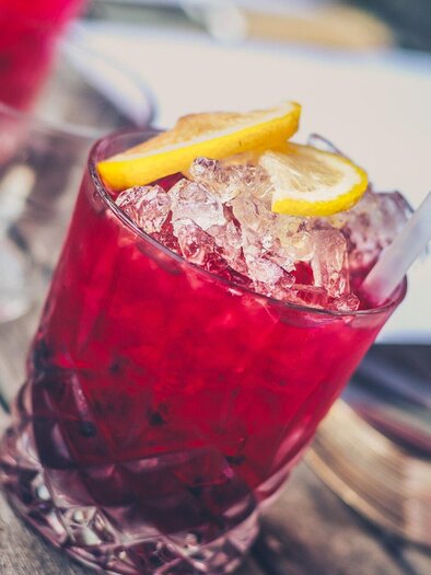 A red cocktail with ice and lemon slices. The drink is on a wooden table and looks refreshing. | © Pixabay