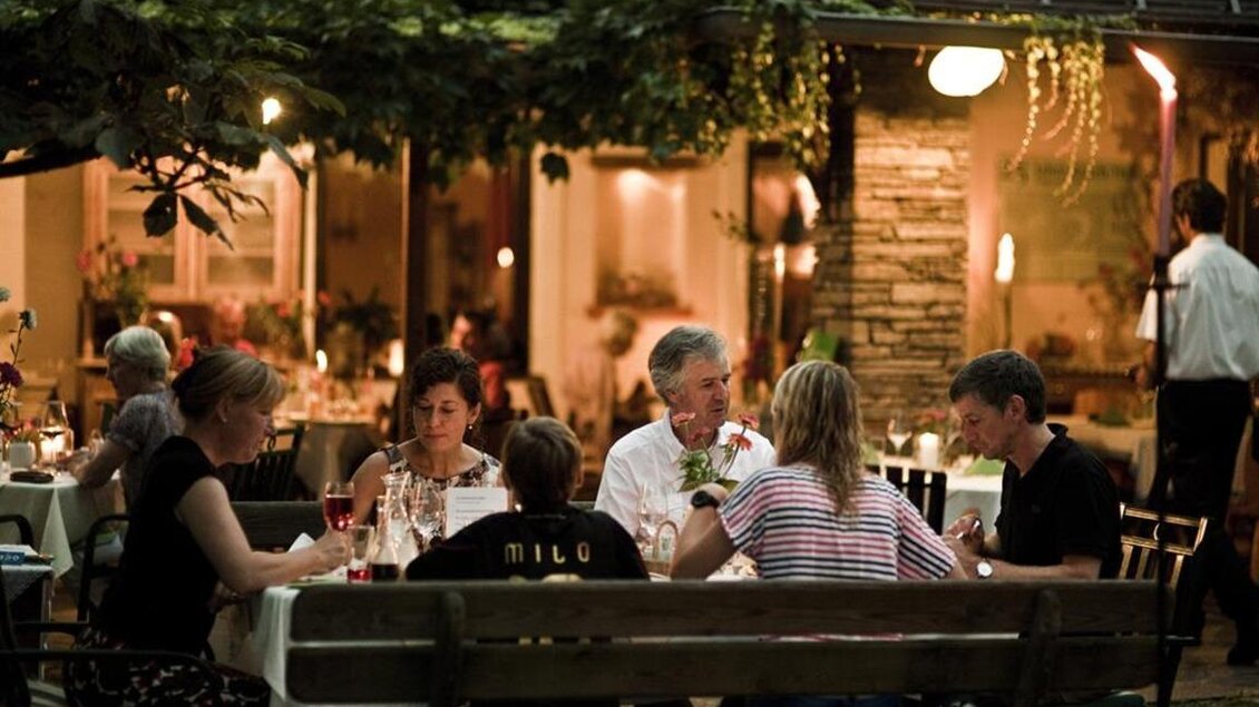 Eine Gruppe von Personen sitzt an einem Tisch im Freien und genießt ein Abendessen. Die Umgebung ist gemütlich und atmosphärisch beleuchtet. | © Rauch-Hof