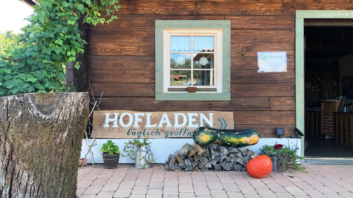 Ein rustikaler Hofladen mit einem Holzschild und einer gemütlichen Atmosphäre. Vor dem Laden liegen Holzscheite und dekorative Kürbisse. | © Kurkommission Bad Blumau