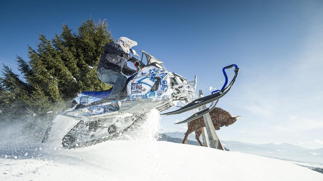 Ein Fahrer auf einem Schneemobil fährt durch den frischen Schnee. Im Hintergrund sind Bäume und ein Hügel zu sehen. | © Philip Platzer
