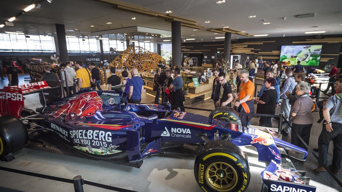 Ein Formel-1-Rennwagen steht in einem modernen Ausstellungsraum. Viele Besucher sind um das Auto versammelt und betrachten die Ausstellung. | © Philip Platzer