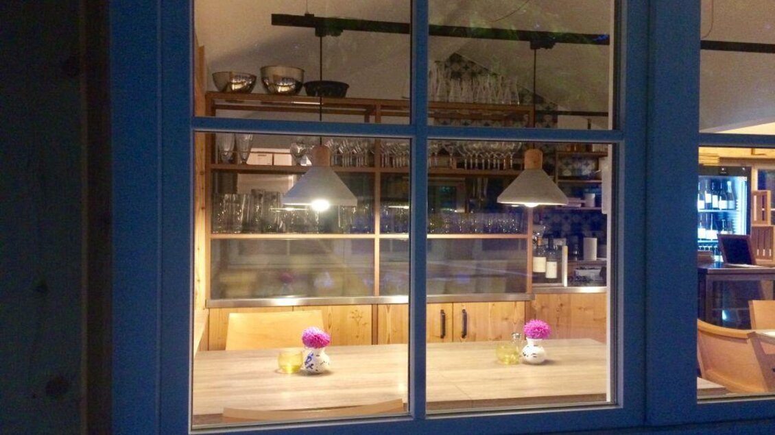 Ein gemütlicher Essbereich mit einem großen Tisch und Hängelampen. Auf dem Tisch stehen Blumenvasen, und die Wände sind mit Gläsern und Geschirr dekoriert. | © Robert Hocker