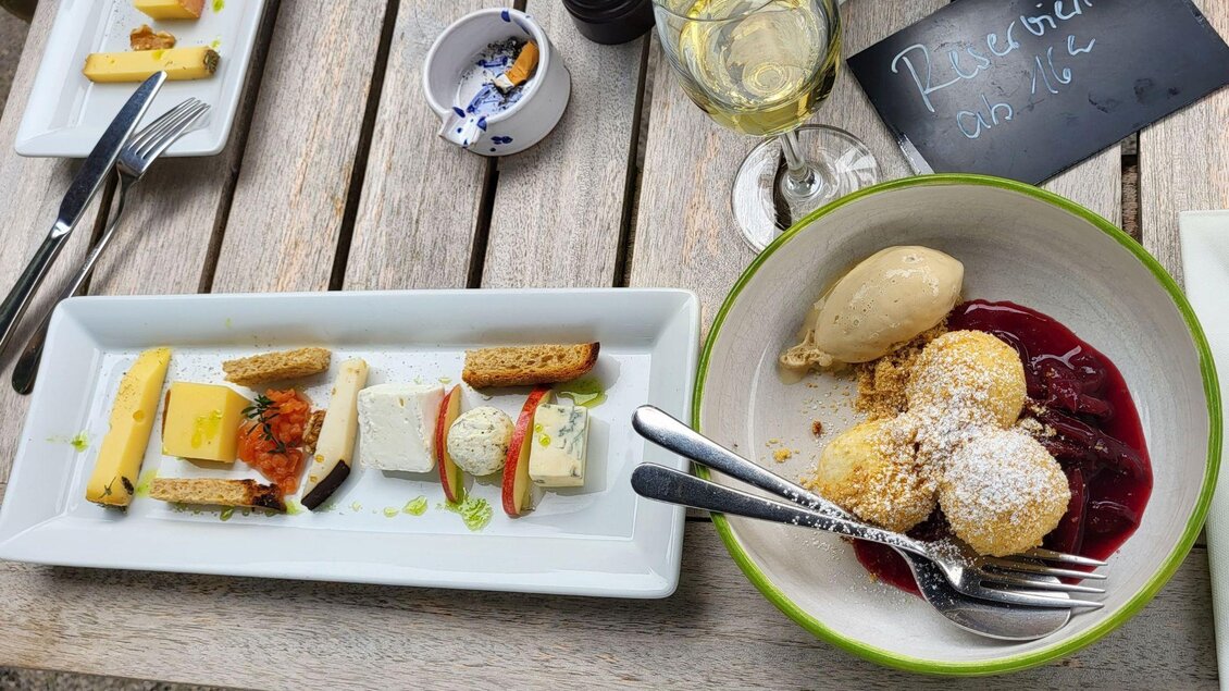 Ein schön angerichtetes Dessert mit drei Kugeln Eis, Beeren und Biskuit. Daneben ein Teller mit verschiedenen kleinen Köstlichkeiten und einem Glas Wein. | © Petra Kirchschlager