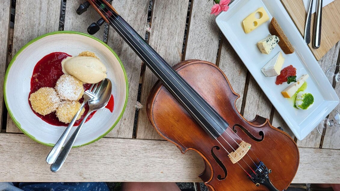 Ein Tisch mit einem Geigeninstrument und zwei Tellern. Auf einem Teller sind Desserts und auf dem anderen verschiedene Käsesorten. | © Petra Kirchschlager
