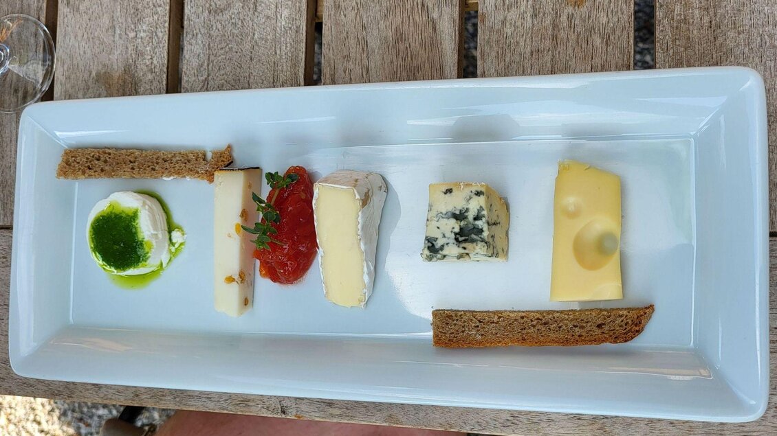 Ein schönes Käsegericht auf einem weißen Teller, mit verschiedenen Käsesorten, Brot und einer grünen Soße. Die Präsentation ist ansprechend und appetitlich. | © Petra Kirchschlager