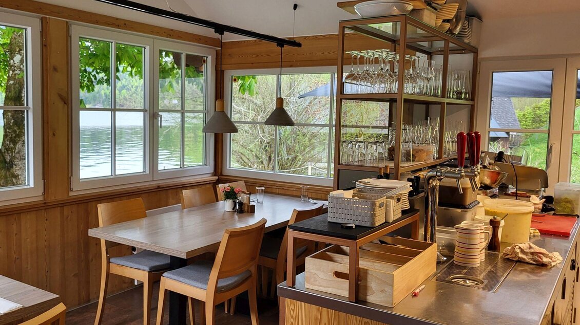 Ein gemütliches Restaurant mit Holzmöbeln und einem Blick auf einen See. Die Fenster lassen viel Licht herein und schaffen eine einladende Atmosphäre. | © Petra Kirchschlager