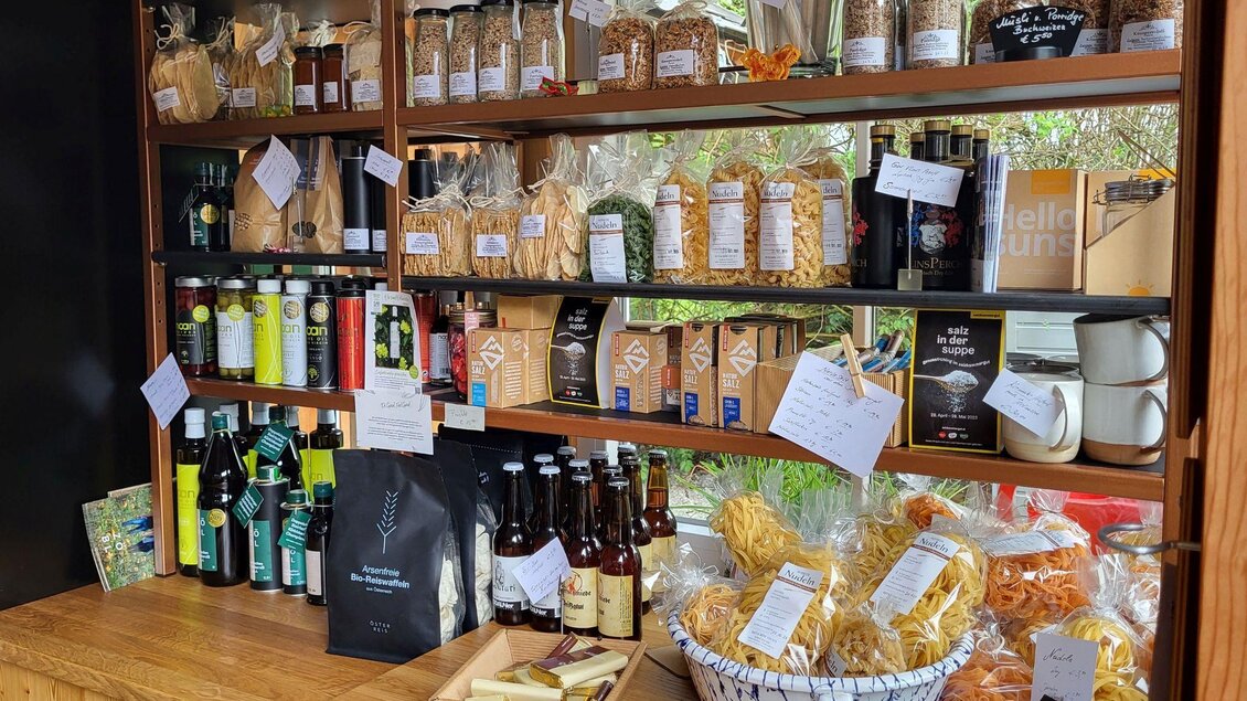 Ein Holzregal voller Lebensmittel und Getränke. Es gibt verschiedene Flaschen, Gläser und Trockenwaren, die ordentlich präsentiert sind. | © Petra Kirchschlager