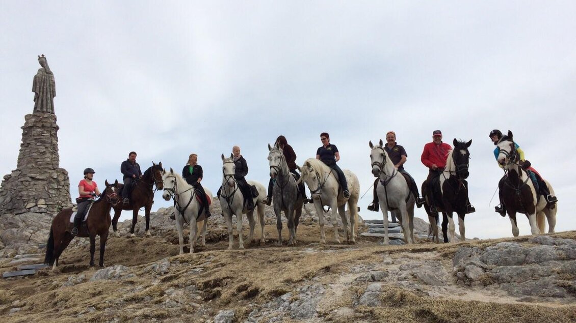 Eine Gruppe von Reitern steht auf einem Hügel neben einer Statue. Der Himmel ist bewölkt und die Landschaft wirkt ruhig. | © Spatenhof