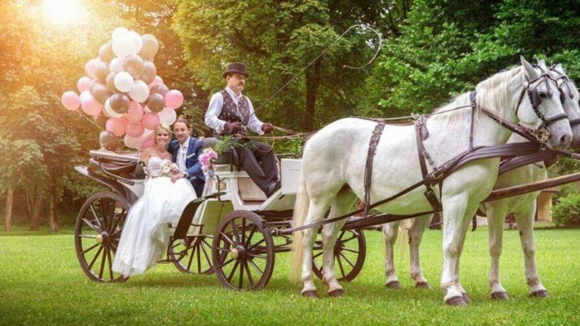 Eine Hochzeit mit einem festlich dekorierten Pferdewagen im Grünen. Das Brautpaar sitzt mit bunten Luftballons auf dem Wagen. | © Spatenhof