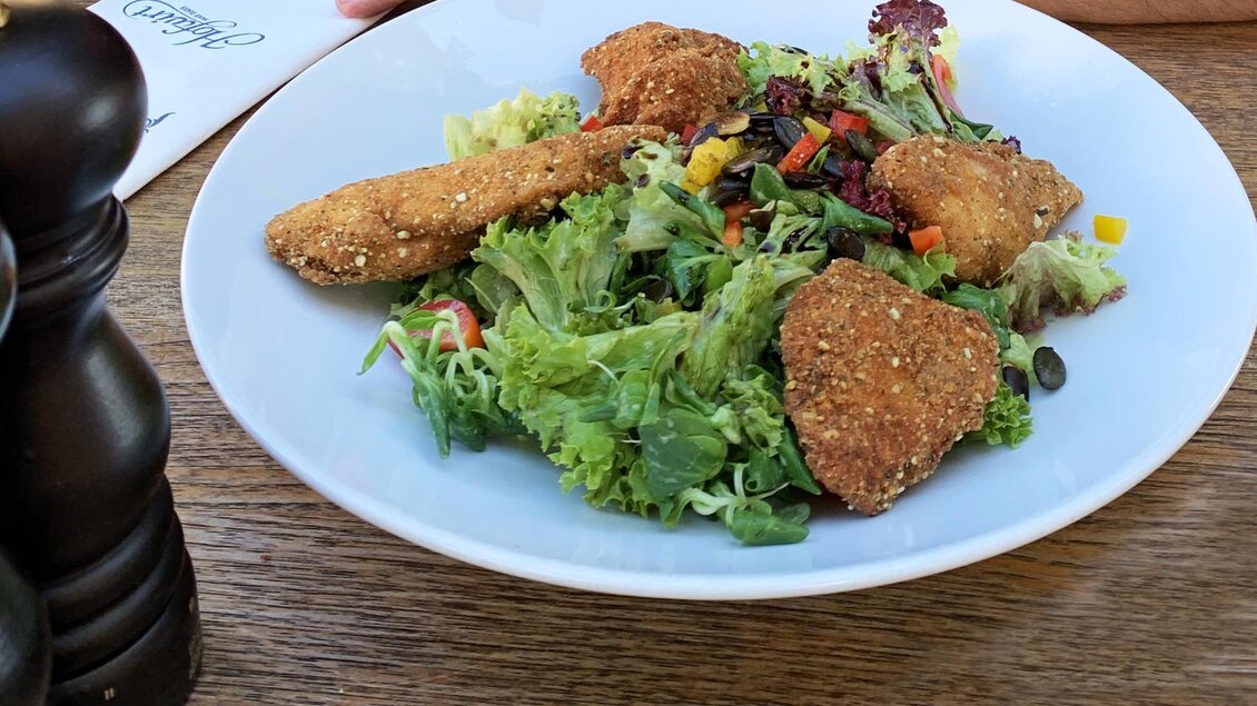 Ein Teller mit frischem Salat und paniertem Hähnchen. Daneben ist ein Stück Pfeffermühle zu sehen. | © Tauroa GmbH