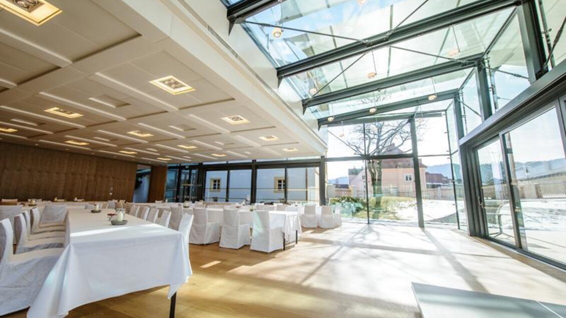 Ein hell erleuchteter Veranstaltungsraum mit großen Fenstern und modernem Design. Tische sind festlich eingedeckt, und die Aussicht ins Freie ist einladend. | © Tauroa GmbH