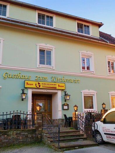 Ein Gasthaus mit der Beschriftung „Gasthaus zum Kirchenwirt“ in einer hellgrünen Fassade. Vor dem Gebäude steht ein Lieferwagen, der ebenfalls mit dem Namen des Gasthauses beschriftet ist. | © TVB Ligist