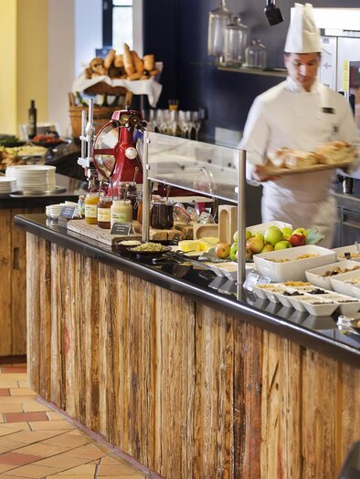A buffet with a variety of food and drinks is visible. A cook is currently preparing the dishes. | © Rogner Bad Blumau