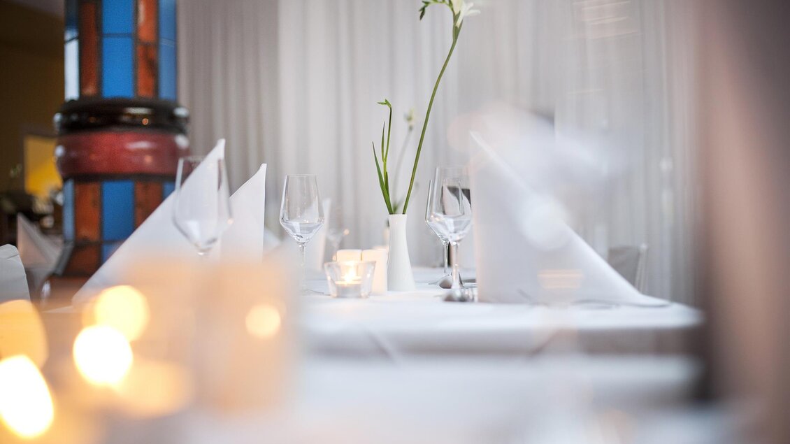 Ein elegant gedeckter Tisch in einem Restaurant mit Gläsern und Servietten. In der Mitte steht eine Vase mit einer Blume. | © Rogner Bad Blumau