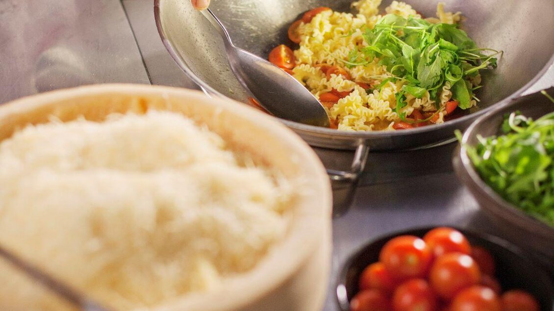 Ein Koch bereitet eine leckere Reisgericht mit frischen Kräutern und Tomaten zu. Im Vordergrund sind Schalen mit Reis und Gemüse zu sehen. | © Rogner Bad Blumau