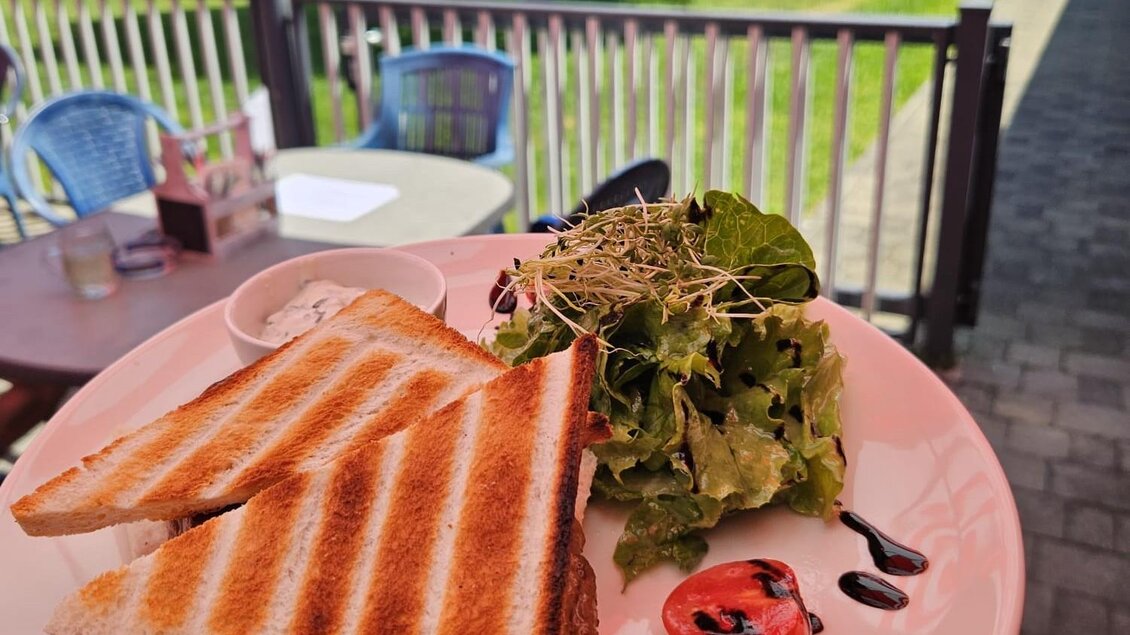 Ein Teller mit geröstetem Brot, gefüllt mit Fleisch, und einem frischen Salat. Im Hintergrund ist ein Schwimmbad und eine grüne Rasenfläche zu sehen. | © Michael Mauser