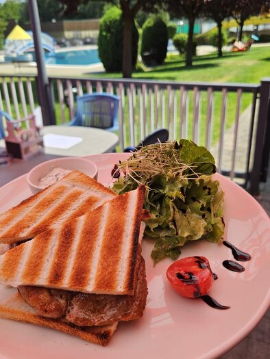Ein Teller mit geröstetem Brot, gefüllt mit Fleisch, und einem frischen Salat. Im Hintergrund ist ein Schwimmbad und eine grüne Rasenfläche zu sehen. | © Michael Mauser