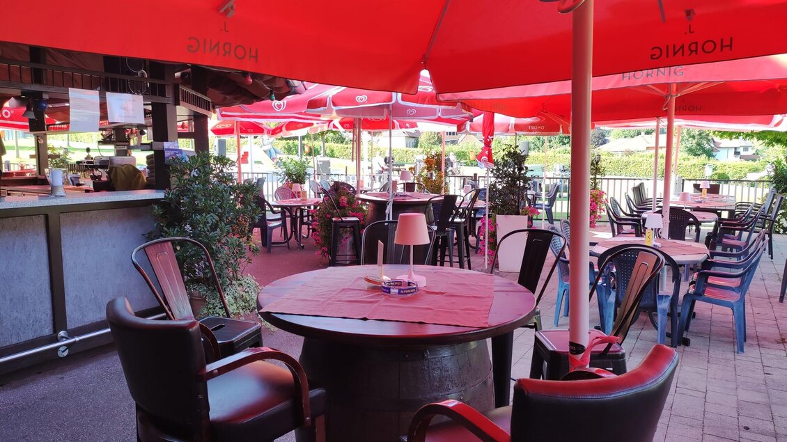 Ein gemütliches Café im Freien mit roten Sonnenschirmen und Tischen. Die Umgebung ist einladend und perfekt für entspannte Stunden im Freien. | © Baresa