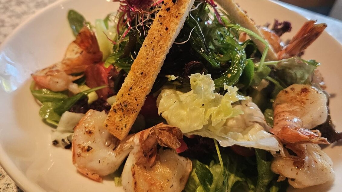 Ein frischer Salat mit Garnelen und verschiedenen Gemüsesorten. Über dem Salat liegen knusprige Croutons. | © Michael Mauser