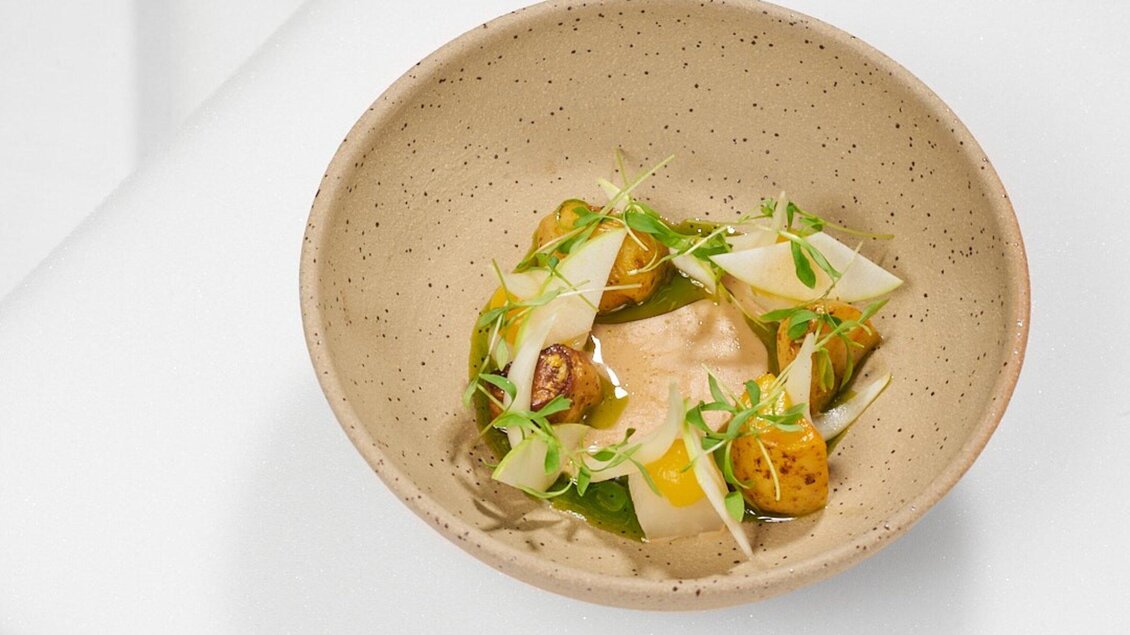 Ein stilvolles Gericht in einer schlichten Schüssel. Es enthält Gemüse, eine cremige Sauce und frische Kräuter. | © Artis