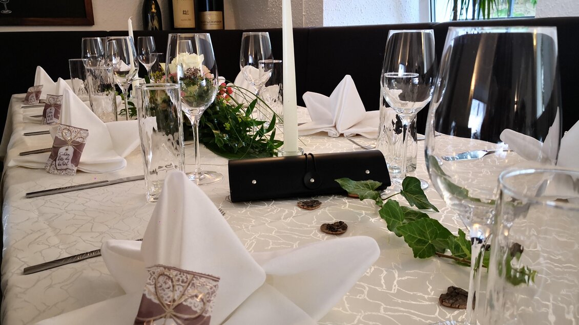 Ein elegant gedeckter Tisch mit Gläsern, Besteck und schön gefalteten Servietten. Die Dekoration umfasst Blumen und Kerzen für eine festliche Atmosphäre. | © Arkadia